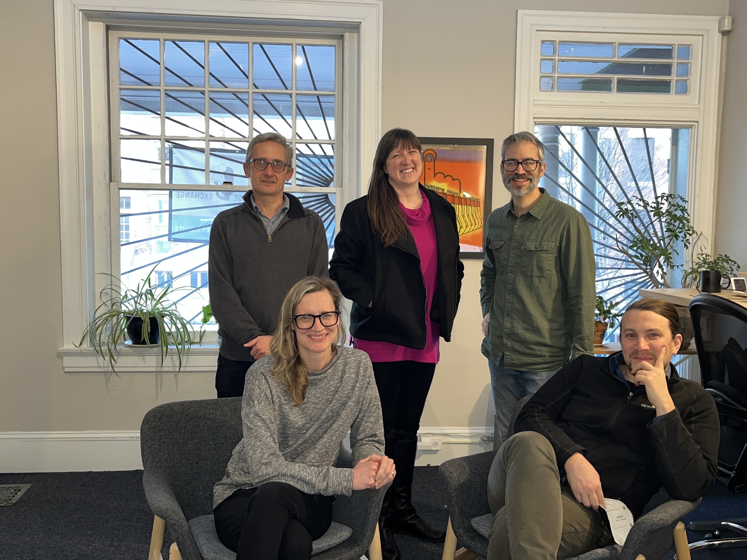 Photo of 5 smiling coworkers in a cozy conference room with windows behind them